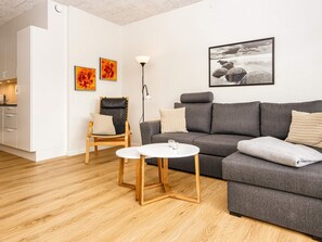 Una sala de estar moderna con un sofá gris, una silla de madera, una mesa de centro blanca y obras de arte en las paredes.