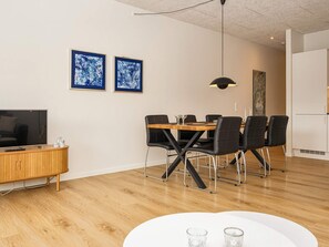 A modern dining area with a wooden table, black chairs, and a TV on a wooden cabinet.