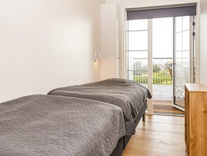 Un dormitorio con dos camas, piso de madera, balcón con vistas y puerta corrediza de cristal.