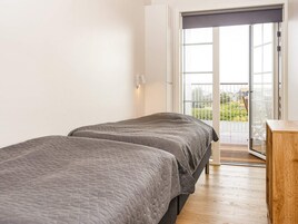 Un dormitorio con dos camas, piso de madera, balcón con vistas y puerta corrediza de cristal.