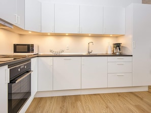 A modern kitchen with white cabinetry, a microwave, a coffee maker, and a sink.