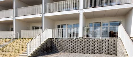 A multi-story building with a flat roof, balconies, and a gravel driveway leading to a set of stairs.
