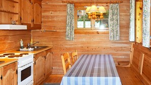 Ein Interieur einer Holzhütte mit Küche, Esstisch und einem Fenster mit Vorhängen.