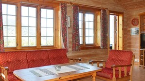 Ein gemütliches Blockhaus-Interieur mit Holztisch, roter Polsterbank und einem Streifenmuster-Teppich.