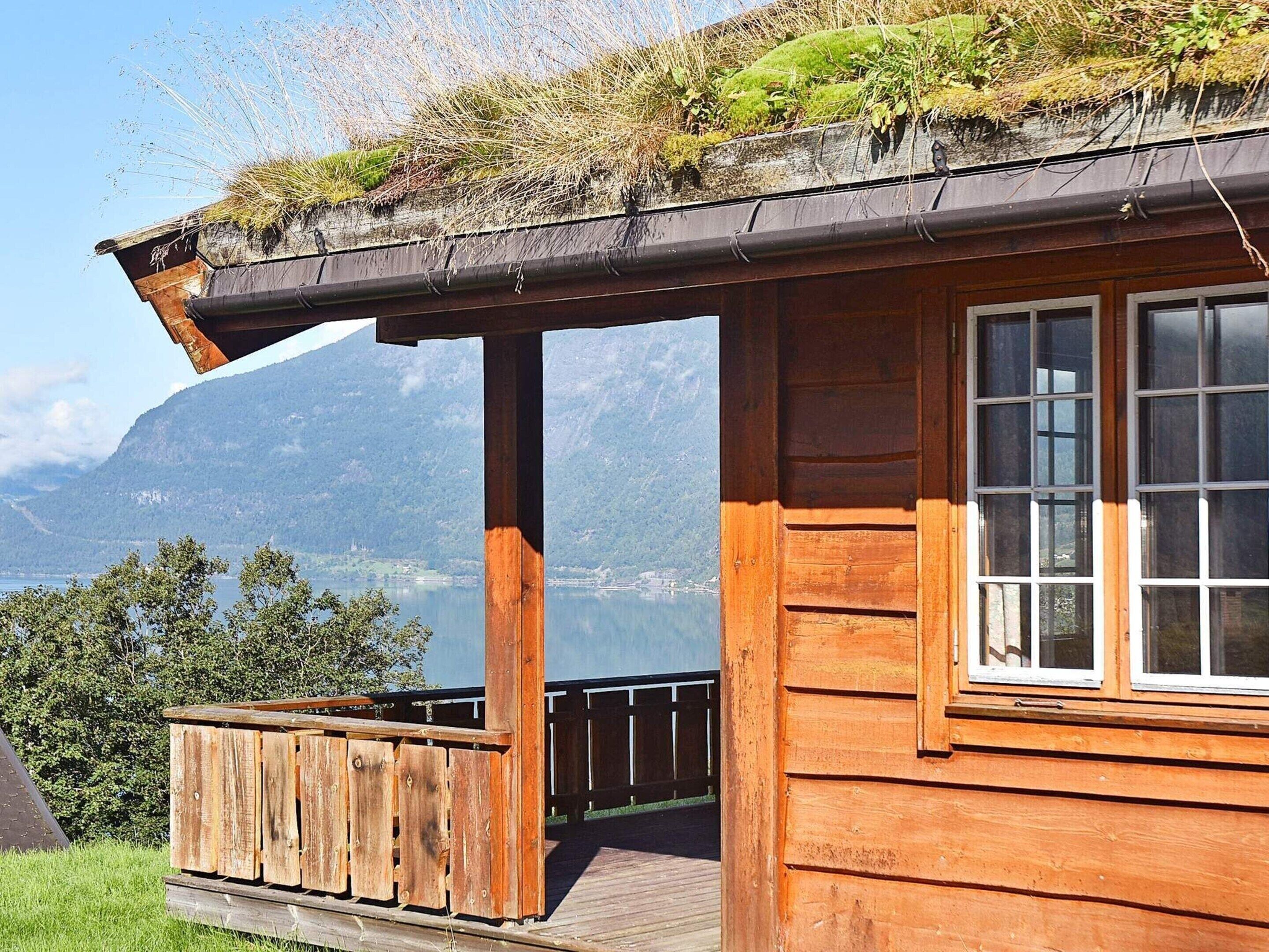Uma cabana de madeira com varanda, dando vista para um lago e montanhas.