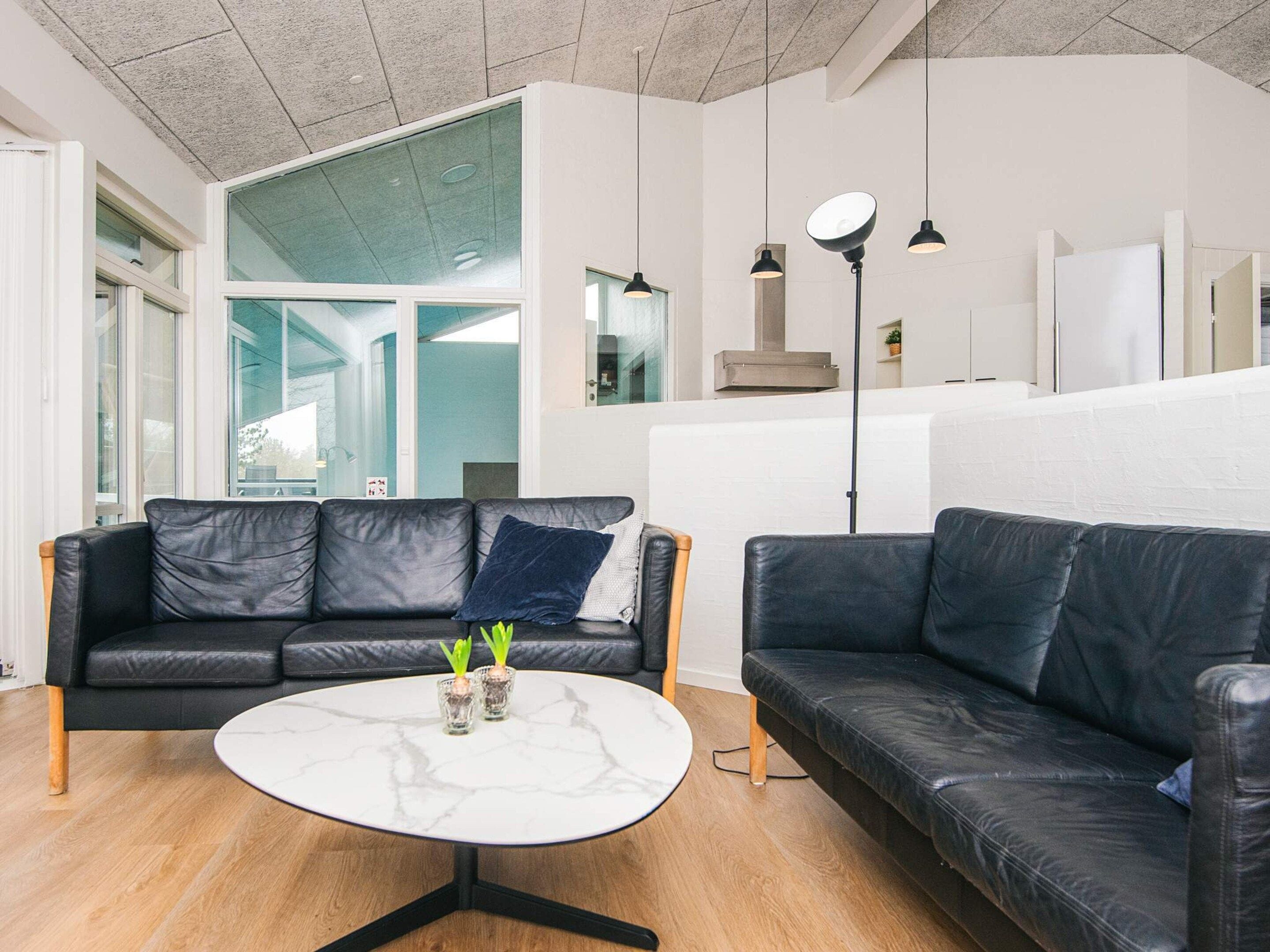 A modern living room with a black leather sofa, a round marble coffee table, and pendant lighting.