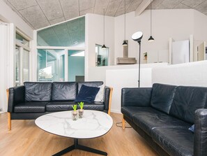 Un salon moderne avec un canapé en cuir noir, une table basse ronde en marbre et des luminaires suspendus.