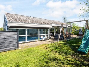 A modern house with a large glass-enclosed patio, a swimming pool, and a slide.