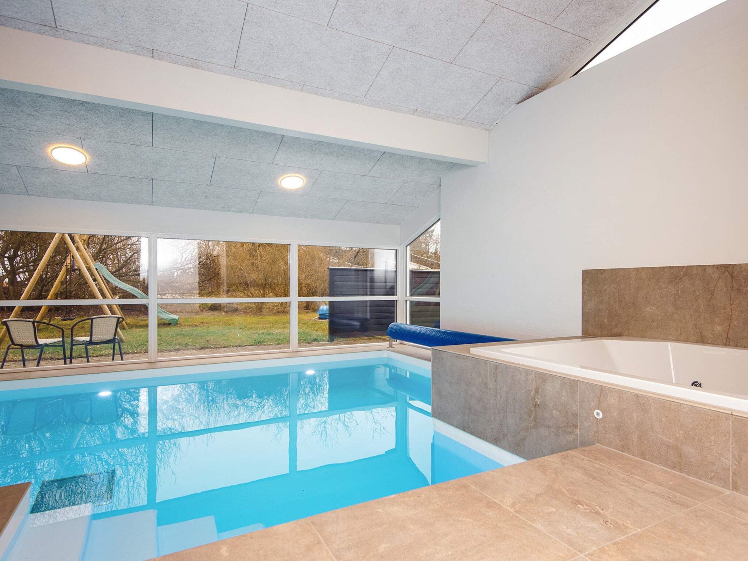 A swimming pool with a hot tub, a swing set, and a view of the outdoors.