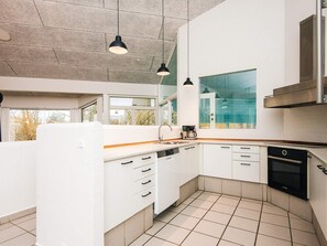 A modern kitchen with white cabinets, a dishwasher, an oven, and a large window offering a view of the outdoors. - 12 Person Holiday Home in Ebeltoft (Ebeltoft)