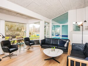 Una sala de estar moderna con vistas a una piscina, que incluye un sofá de cuero negro, una mesa de centro redonda y un comedor con mesa y sillas de madera.