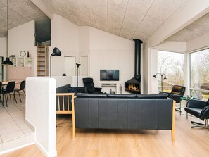 A modern living room with a black leather sofa, a fireplace, a TV, and a dining area with chairs and a table. - 12 Person Holiday Home in Ebeltoft (Ebeltoft)