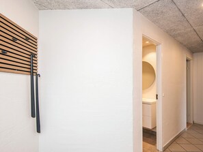 A hallway with a white wall, a wooden slat wall art piece, and a door leading to a room with a round mirror and a white cabinet.