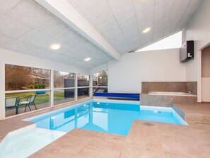 Une piscine intérieure avec des parois en verre transparent, un sol carrelé et un banc intégré.