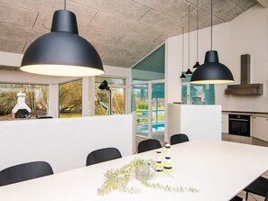 A modern kitchen with a large island, pendant lighting, and a view of a backyard with a swing set. - 12 Person Holiday Home in Ebeltoft (Ebeltoft)