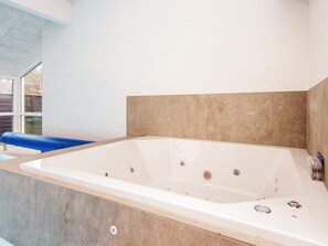 A modern bathroom with a large bathtub, a blue bench, and a window providing natural light. - 12 Person Holiday Home in Ebeltoft (Ebeltoft)