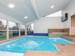 An indoor swimming pool with clear glass walls, a blue water feature, and a sauna area. - 12 Person Holiday Home in Ebeltoft (Ebeltoft)