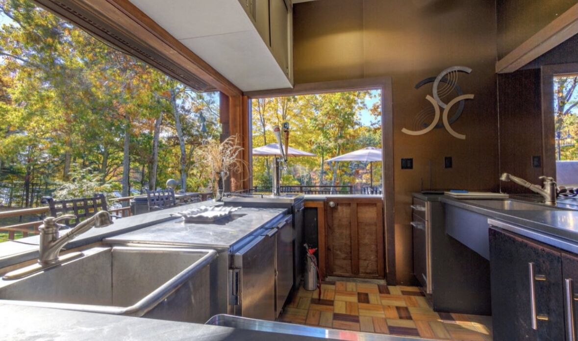 A modern kitchen with a large window, wooden flooring, and a view of trees.