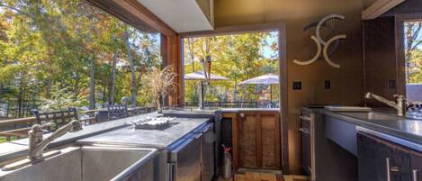 A modern kitchen with a large window, wooden flooring, and a view of trees.