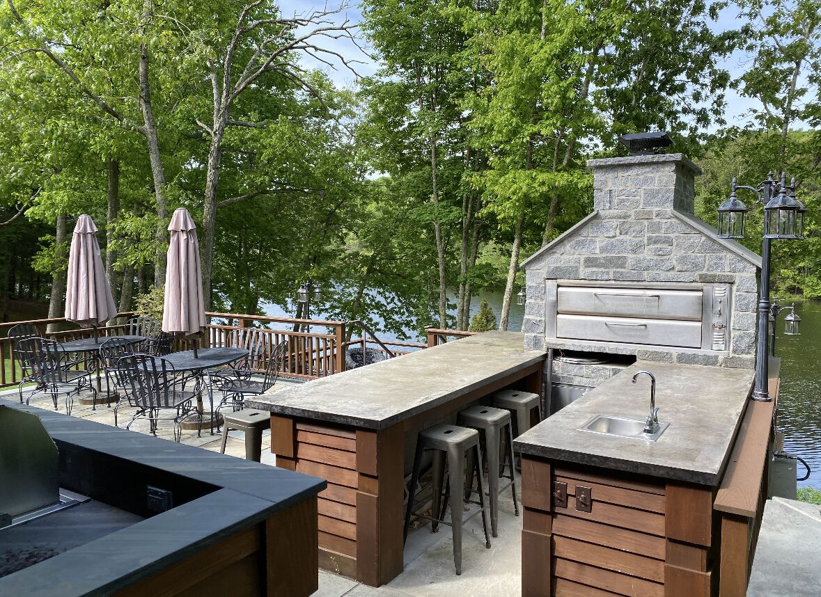 An outdoor kitchen area with a stone chimney, bar stools, and a grill.