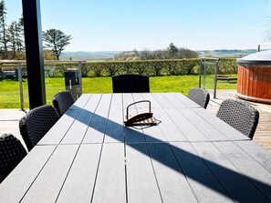 An outdoor patio with a table and chairs, a hot tub, and a view of the countryside.