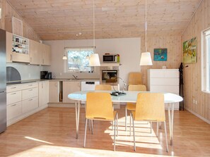 Moderni keittiö, jossa on puiset kaapit, ruokapöytä tuoleineen ja jääkaappi.