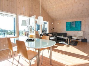 A spacious living area with a high ceiling, a dining table with chairs, a sofa, a coffee table, and a large window offering a view.