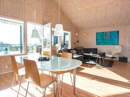 Amplia sala de estar con techo alto, una mesa de comedor con sillas, un sofá, una mesa auxiliar y un gran ventanal con vistas.
