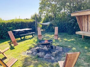 Ett utomhusområde med en eldstad, ett picknickbord och träkonstruktioner.