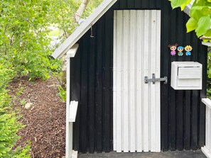 Mustavalkoinen varasto, jossa on saranalla kiinnitetty ovi, pieni valkoinen sähkökaappi ja metallinen salpa.