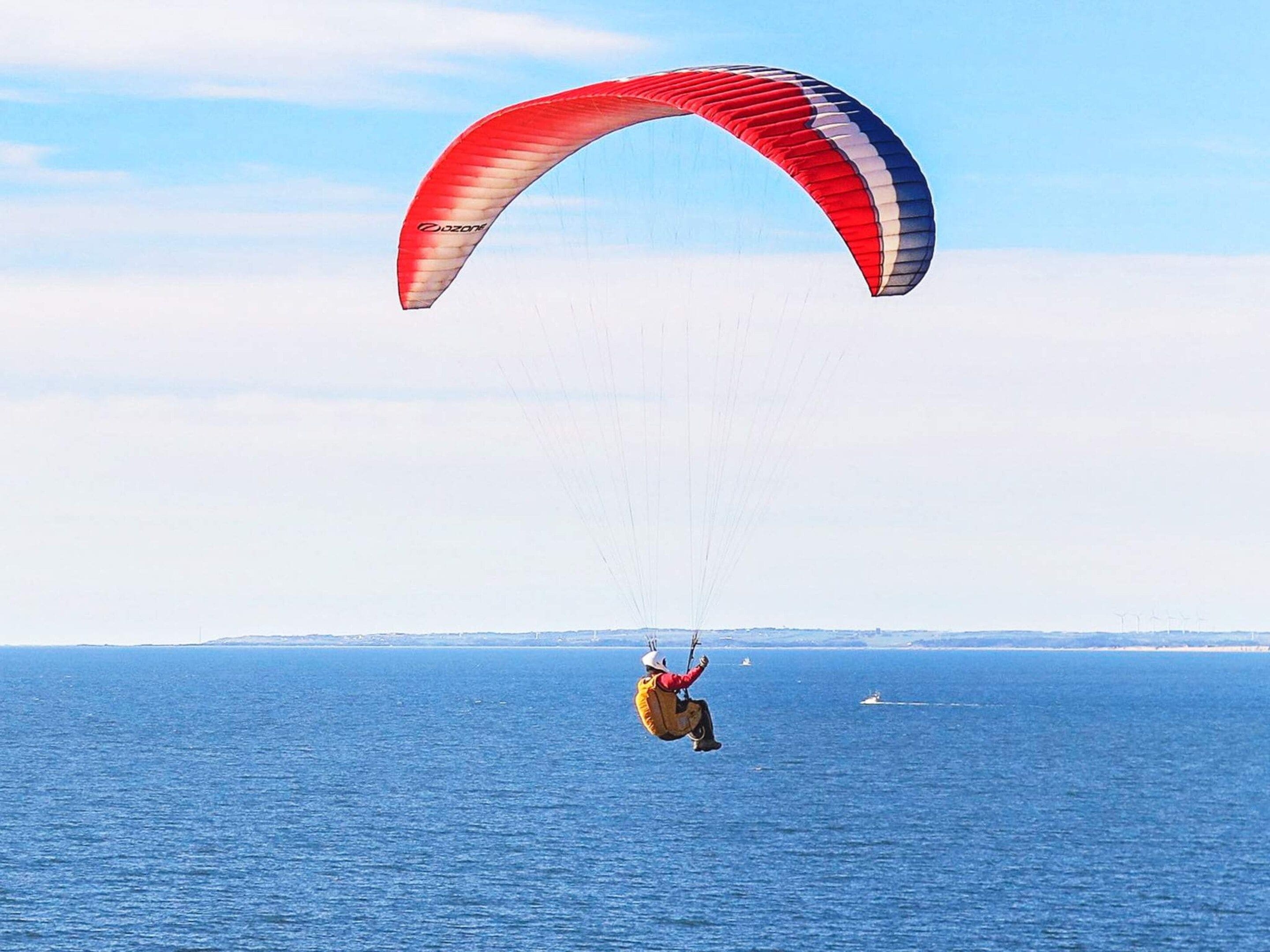 A person paragliding over a body of water with a clear sky and distant land in the background.