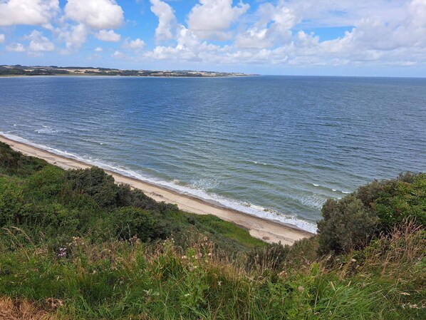 A coastal landscape with a beach, ocean, and distant land.