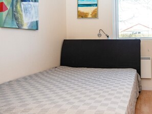 Une chambre à coucher avec un lit, une fenêtre, une lampe fixée au mur et un tableau.