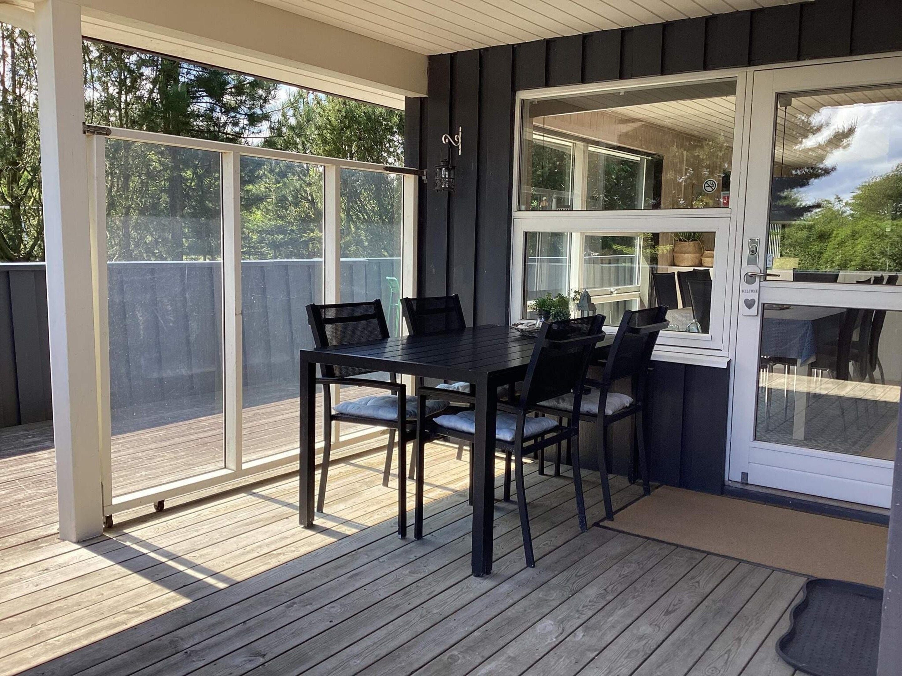 A deck with a table and chairs, a sliding glass door, and a view of trees.