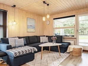 A cozy living room with a dark blue sofa, a white coffee table, and a woven pouf. - 8 Person Holiday Home in Blokhus (Blokhus)