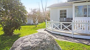 Une maison en bois blanche, dotée d’un porche, avec un gros rocher au premier plan et un arbre aux fleurs roses.
