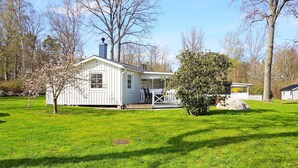 Une maison blanche d’un seul étage, dotée d’un porche, entourée d’une pelouse bien entretenue et d’arbres.