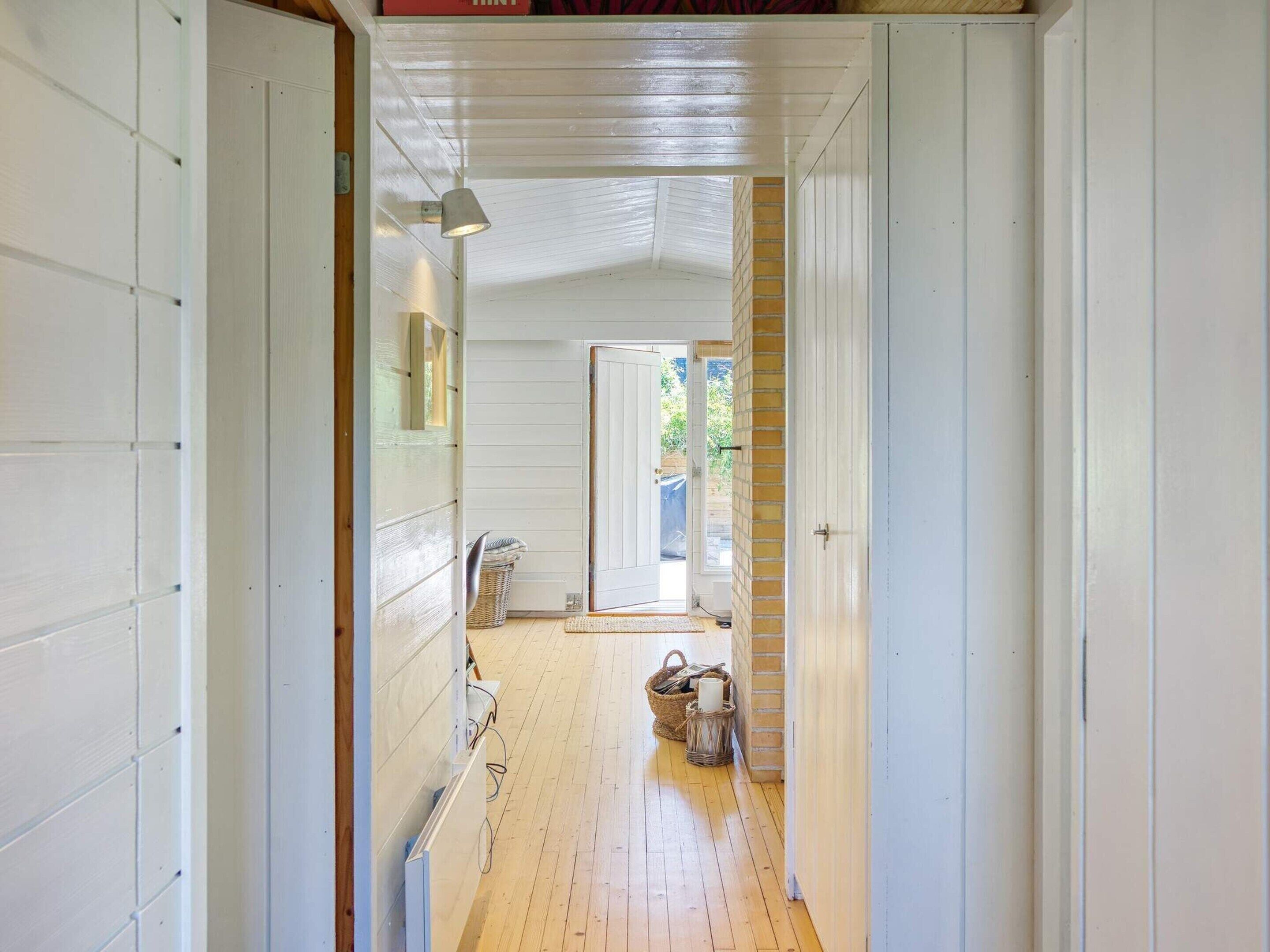 A narrow hallway with wooden flooring, white walls, and a door leading to an outdoor area.