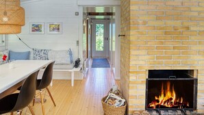 Una habitación acogedora con chimenea de ladrillo, una mesa de comedor con sillas, un sofá y un pasillo que conduce a una puerta.