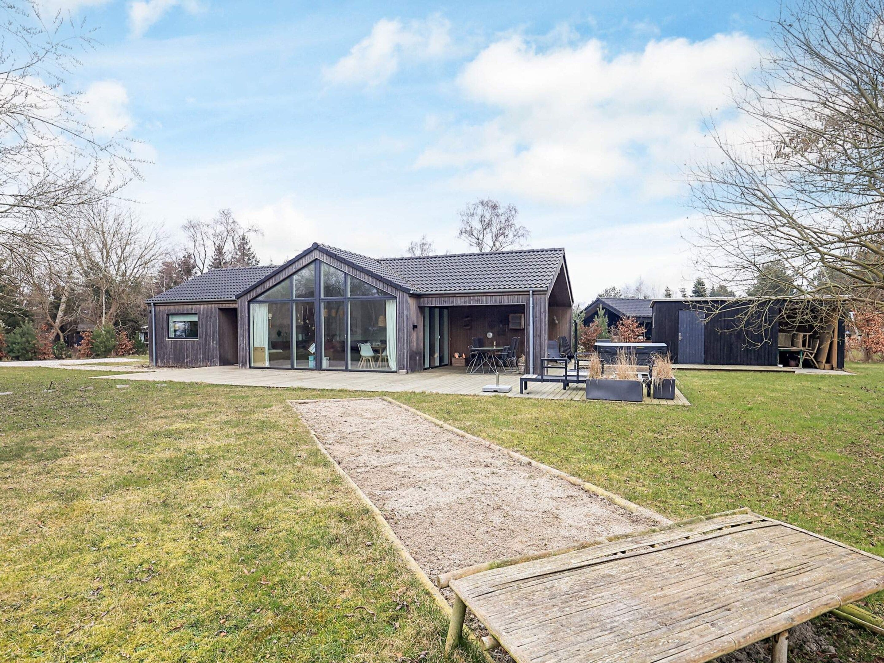 Une maison moderne dotée d’une grande baie vitrée, d’une terrasse en bois et d’une cour gazonnée.