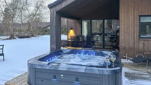 A hot tub outside a wooden building with a glass door, surrounded by snow. - 5 Star Holiday Home in Vaeggerlose (Vaeggerlose)