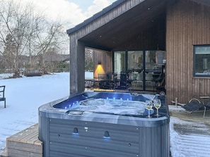 A hot tub outside a wooden building with a glass door, surrounded by snow. - 5 Star Holiday Home in Vaeggerlose (Vaeggerlose)