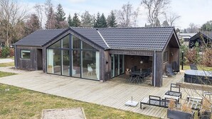 A modern house with a large glass window, a wooden deck, and a patio area. - 5 Star Holiday Home in Vaeggerlose (Vaeggerlose)