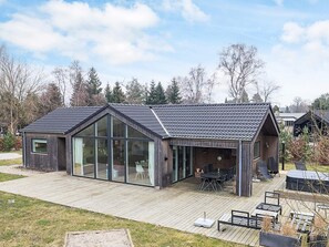 A modern house with a large glass window, a wooden deck, and a patio area. - 5 Star Holiday Home in Vaeggerlose (Vaeggerlose)