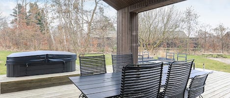 Un patio exterior con terraza de madera, un jacuzzi, y sillas y mesas de metal negro.