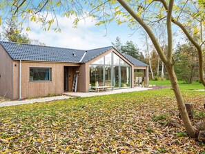 Ein modernes Haus mit einem großen Glasfenster, einer Holzfassade und einem überdachten Sitzbereich im Freien.
