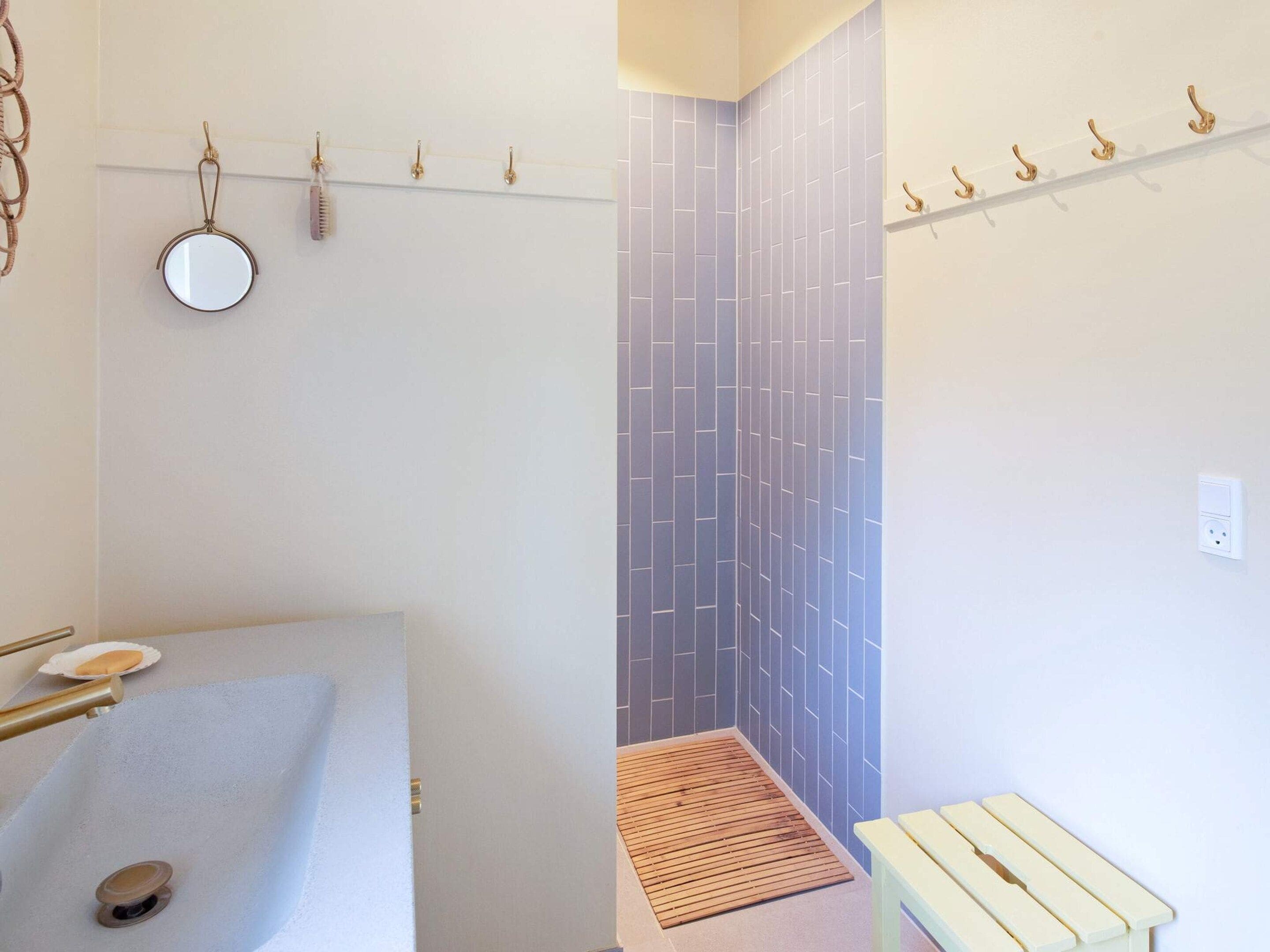 Une salle de bain avec un lavabo blanc, un miroir et un espace douche doté d’un sol en bois.