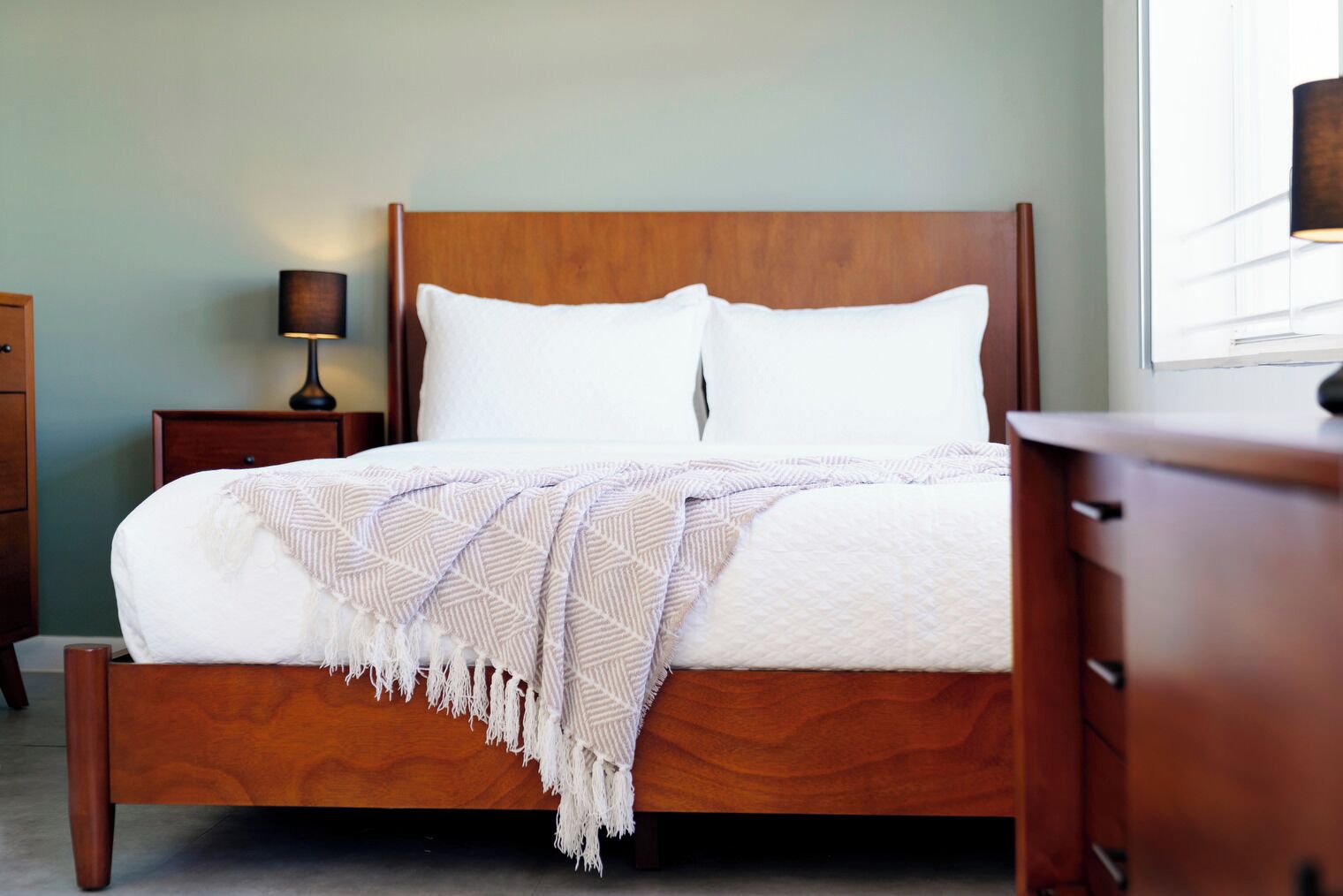 A neatly made bed with a patterned throw blanket, a wooden headboard, and a nightstand with a lamp.