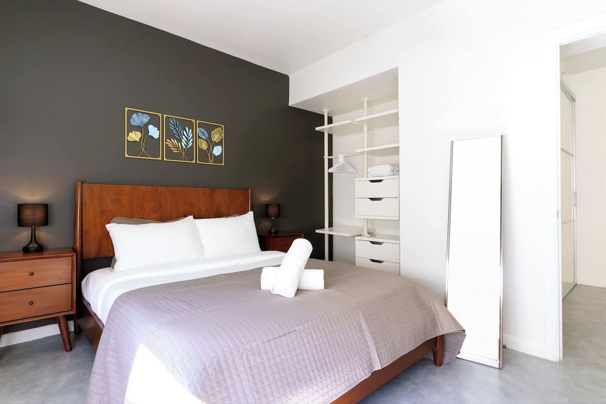 A neatly made bed with white linens, a wooden headboard, and a bedside table with a lamp.