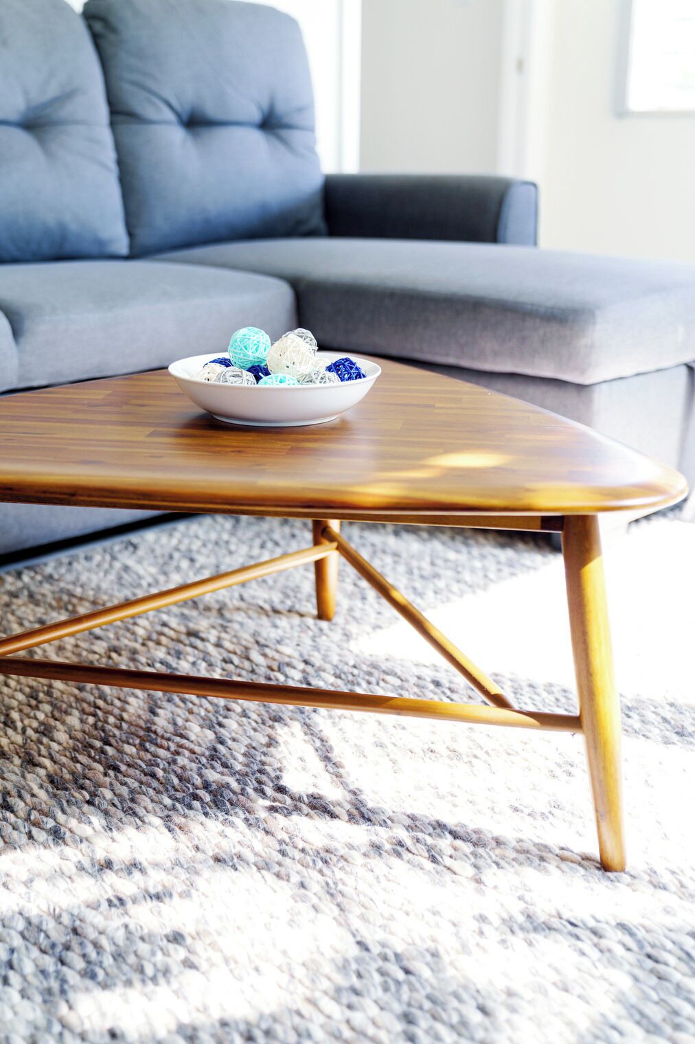Ein modernes Wohnzimmer mit einem Holztisch, einem grauen Sofa und einem gemusterten Teppich.